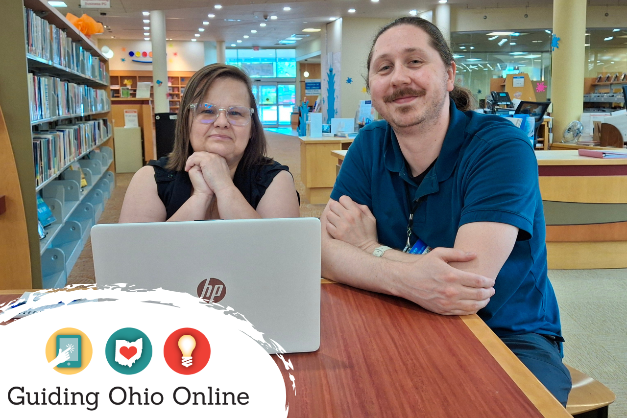 A smiling man and a woman sitting at a table with a laptop computer.